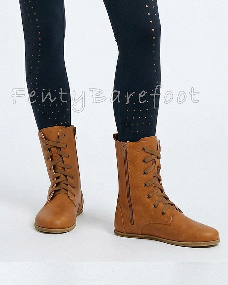 Op de afbeelding: Tan leren veterlaarzen met zijritsen. De laarzen hebben een platte zool en worden gedragen met donkere leggings. De tekst "FentyBarefoot" is zichtbaar op de leggings.