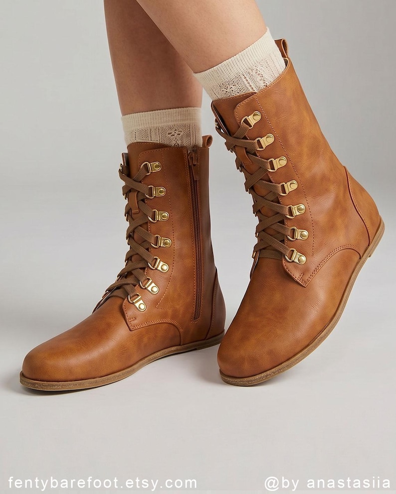 May include: Brown leather boots with a lace-up design and gold-tone eyelets. The boots have a side zipper and are worn with cream-colored socks. The boots are flat-soled and have a classic, rugged style. The Etsy shop name is visible at the bottom of the image.