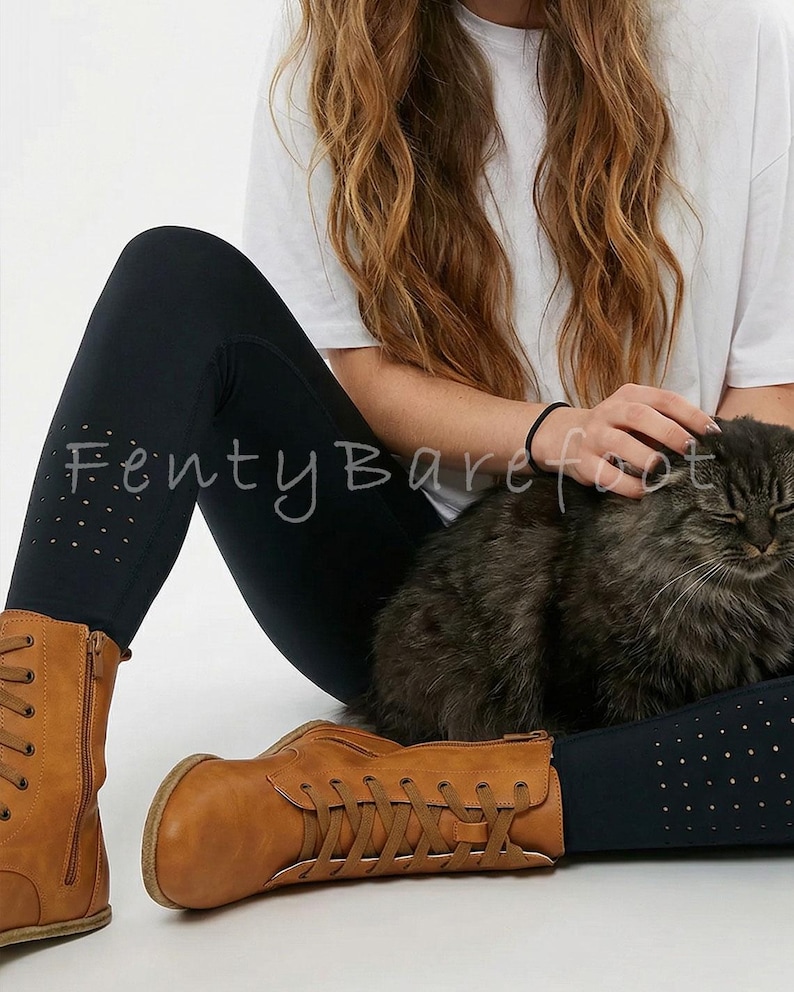 Op de afbeelding: Zwarte legging met geperforeerde details en bruine leren laarzen met veters en ritsen. De tekst "Fenty Barefoot" is zichtbaar op de legging. Een pluizige kat ligt op schoot.