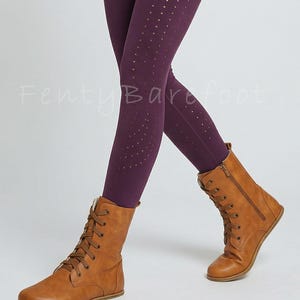 Op de afbeelding: Bruine veterlaarzen met een zijrits, gecombineerd met donkerpaarse leggings met kleine perforaties. De tekst "Fenty Barefoot" is zichtbaar. De laarzen lijken van leer te zijn.