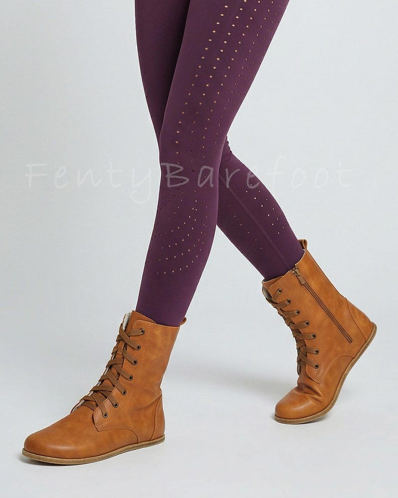 Op de afbeelding: Bruine veterlaarzen met een zijrits, gecombineerd met donkerpaarse leggings met kleine perforaties. De tekst "Fenty Barefoot" is zichtbaar. De laarzen lijken van leer te zijn.