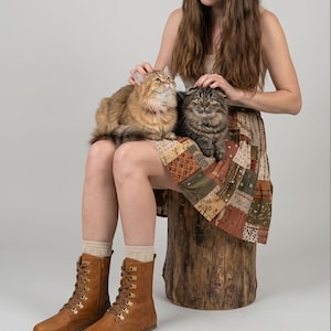 May include: A person sits with two cats, one brown and one gray, on their lap. They wear a patchwork skirt, tan socks, and brown lace-up boots. The boots have gold-colored eyelets. The Etsy shop name "fentybarefoot.etsy.com" is visible.