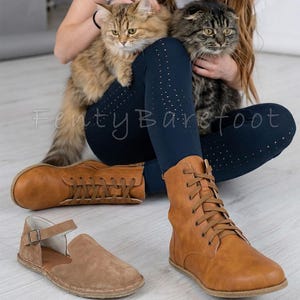 Op de afbeelding: Er worden twee paar schoenen getoond: bruine leren laarzen en bruine su&egrave;de sandalen. De laarzen zijn geregen en hoog, terwijl de sandalen een bandje en een gesp hebben. De tekst "Fenty Barefoot" is zichtbaar.