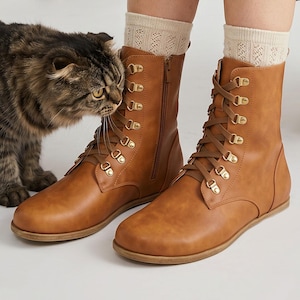 May include: Brown leather boots with a lace-up design and gold-tone eyelets. The boots have a side zipper and are paired with cream-colored socks. A cat is near the boots. The Etsy shop name is visible at the bottom of the image.