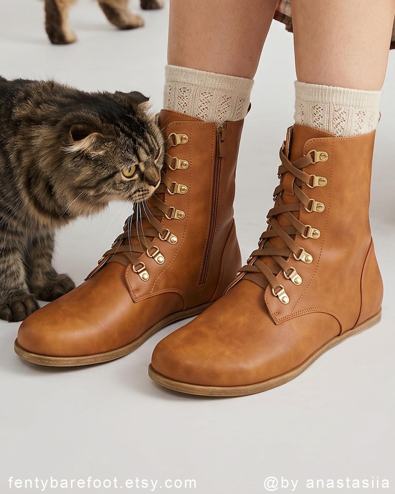 May include: Brown leather boots with a lace-up design and gold-tone eyelets. The boots have a side zipper and are paired with cream-colored socks. A cat is near the boots. The Etsy shop name is visible at the bottom of the image.