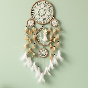 May include: A handcrafted dreamcatcher with a circular woven design, featuring a central crescent moon and star, adorned with feathers in shades of white and brown. The dreamcatcher is suspended by a natural fiber cord, creating a bohemian aesthetic.