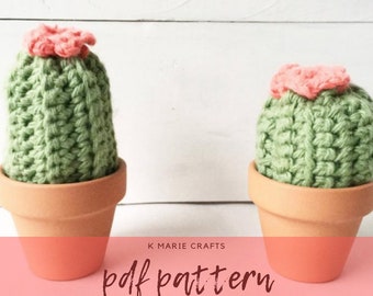 May include: Two crocheted cactus plants in terracotta pots. The cactus plants are green with pink flowers on top. The image has the text "K Marie Crafts pdf pattern" at the bottom.