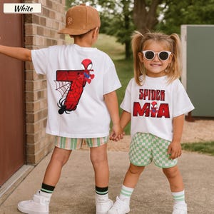 May include: Two children wearing white t-shirts with Spider-Man graphics. One shirt features a red number 7 with a spider web design, and the other says "Spider Mia" in red letters. They are wearing shorts and sneakers.