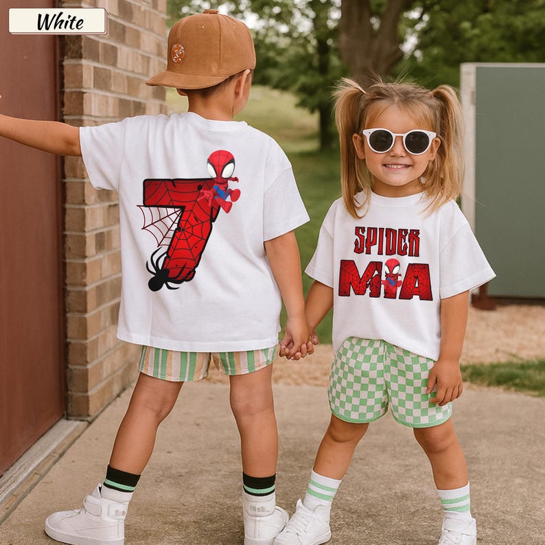 May include: Two children wearing white t-shirts with Spider-Man graphics. One shirt features a red number 7 with a spider web design, and the other says "Spider Mia" in red letters. They are wearing shorts and sneakers.
