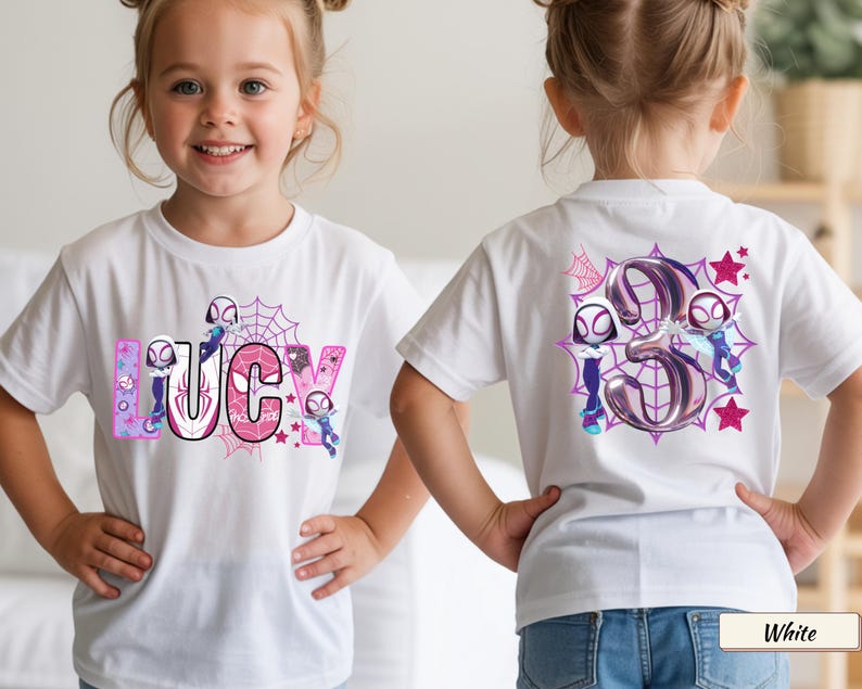 K&ouml;nnte beinhalten: Wei&szlig;es T-Shirt mit dem Namen "LUCY" in rosa und lila Buchstaben, Spinnennetz-Design und Cartoon-Figuren. Auf der R&uuml;ckseite des Shirts ist eine gro&szlig;e "3" mit Spinnennetz- und Sternakzenten abgebildet.