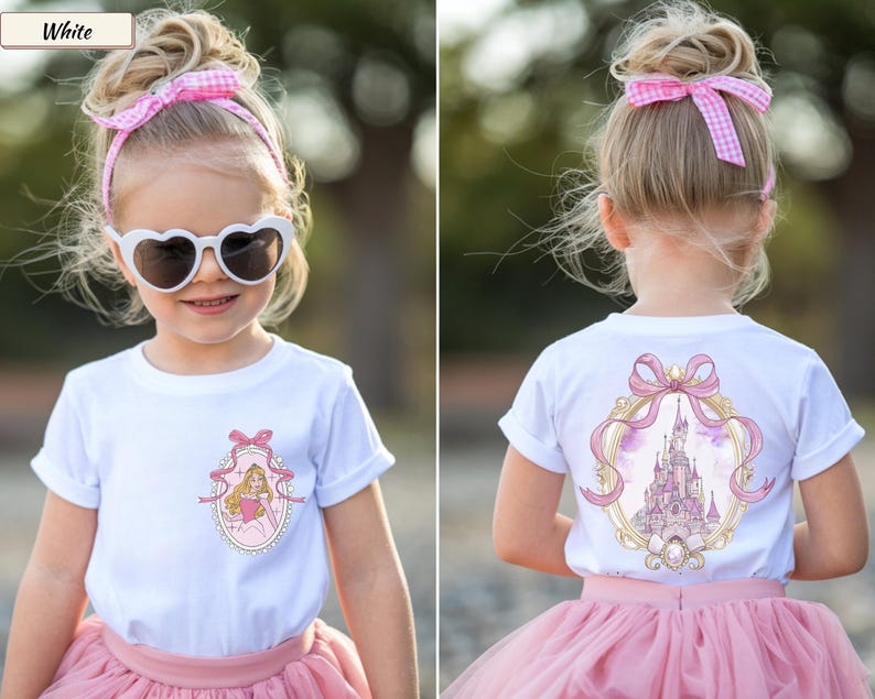 Op de afbeelding: Een wit t-shirt met korte mouwen en een kleine afbeelding op de linkerborst van een prinses in een gouden ovaal frame met een roze strik. De achterkant van het shirt toont een grotere versie van hetzelfde gouden frame met een kasteel.