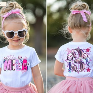 K&ouml;nnte beinhalten: Wei&szlig;es T-Shirt mit dem Namen "MILA" in rosa und lila Buchstaben, mit Spinnennetz- und Superhelden-Grafiken. Auf der R&uuml;ckseite des Shirts befindet sich die Zahl 3 mit Superheldenfiguren und Sternen. Das Kind tr&auml;gt einen rosa T&uuml;llrock und eine Sonnenbrille.