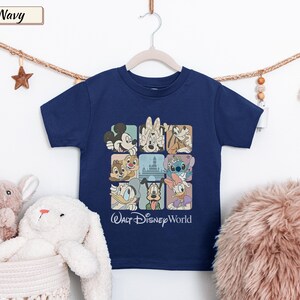 May include: A navy blue short-sleeve t-shirt featuring a grid graphic of various Disney characters including Mickey Mouse, Minnie Mouse, Goofy, Chip, Dale, Stitch, Donald Duck, Pluto, and Daisy Duck, with the text Walt Disney World printed below.