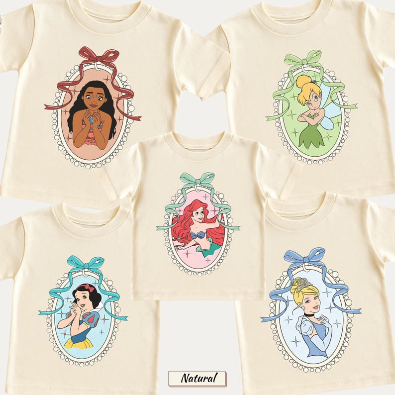May include: Five cream-colored short-sleeve t-shirts featuring oval frames with scalloped edges. Each frame contains a different cartoon character: Moana with a red bow, Tinker Bell with a green bow, Ariel with a teal bow, Snow White with a blue bow, and Cinderella with a light blue bow.