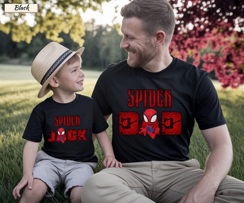 May include: Black t-shirts with red Spider-Man graphics. One shirt says "Spider Dad" with a Spider-Man character, and the other says "Spider Jack" with a Spider-Man character. A child wears a straw hat and gray shorts.