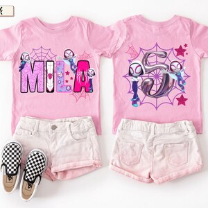 K&ouml;nnte beinhalten: Zwei rosa T-Shirts mit passenden Shorts und Schuhen. Ein Shirt zeigt den Namen "MILA" mit einem Spinnennetz-Design und Zeichentrickfiguren. Das andere Shirt hat eine gro&szlig;e Zahl "5" mit Zeichentrickfiguren und Sternen.