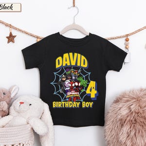 May include: A black short-sleeve t-shirt featuring a graphic of Marvel Spidey and His Amazing Friends characters inside a spiderweb. The text reads DAVID, 4, and BIRTHDAY BOY in yellow and blue lettering on the front of the garment.