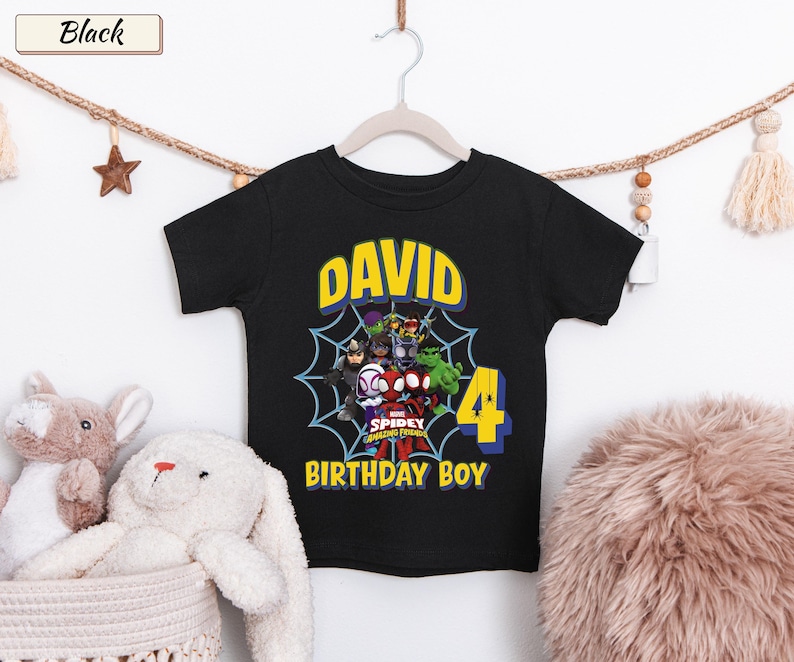 May include: A black short-sleeve t-shirt featuring a graphic of Marvel Spidey and His Amazing Friends characters inside a spiderweb. The text reads DAVID, 4, and BIRTHDAY BOY in yellow and blue lettering on the front of the garment.