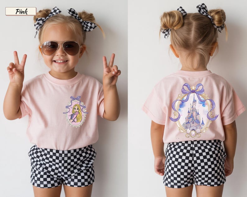 Op de afbeelding: Een lichtroze t-shirt met een kleine afbeelding van een blond personage in een paarse jurk op de linkerborst en een grote afbeelding van een kasteel omlijst door een paarse strik op de achterkant, gecombineerd met zwart-wit geblokte shorts.