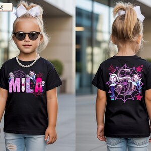 K&ouml;nnte beinhalten: Schwarzes T-Shirt mit dem Namen "MILA" in Rosa und Lila, Spinnennetz- und Cartoon-Charakter-Design. Auf der R&uuml;ckseite befindet sich eine gro&szlig;e "5" mit zwei Charakteren und Spinnennetzen. Das T-Shirt wird von einem Kind getragen.