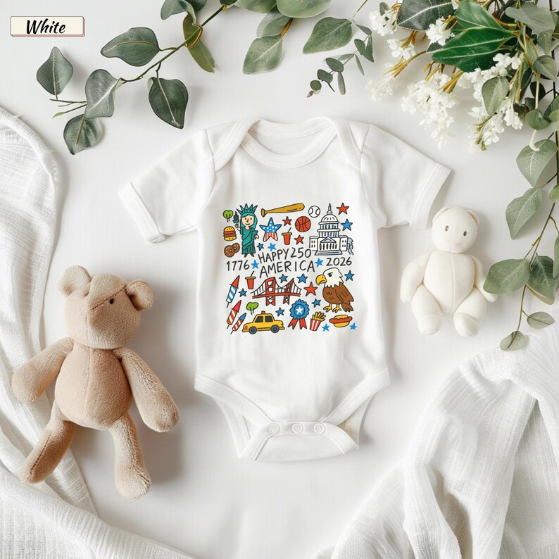 May include: A white short-sleeved baby bodysuit featuring a colorful graphic print of American icons including the Statue of Liberty, a bald eagle, the Capitol building, and a yellow taxi, with the text "HAPPY 250 AMERICA 1776 2026".