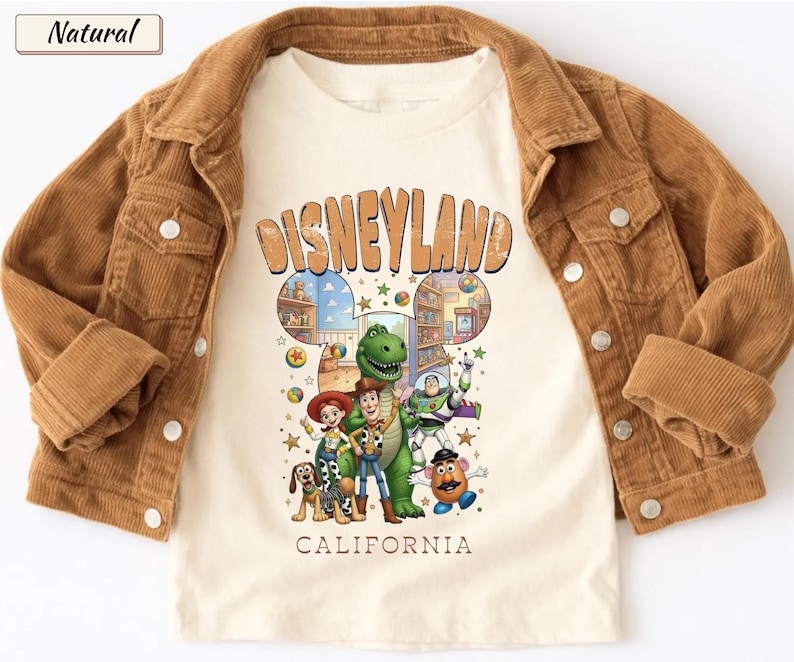 May include: A tan corduroy jacket over a cream-colored t-shirt featuring a Disneyland graphic with cartoon characters. The shirt has the words "Disneyland California" in orange. The jacket has button closures and pockets.