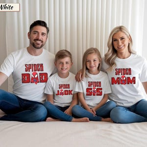 May include: White t-shirts with red and black text that reads "Spider Dad", "Spider Jack", "Spider Sis", and "Spider Mom". The shirts are worn by a family of four, all wearing blue jeans.