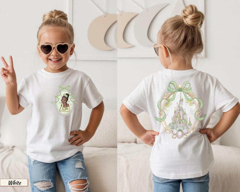 Op de afbeelding: Een wit t-shirt met korte mouwen en een kleine afbeelding op de linkerborst van een prinses in een groene jurk binnen een ovaal kader. De achterkant van het shirt toont een grote illustratie van een kasteel in een sierlijk ovaal kader met een groene strik.