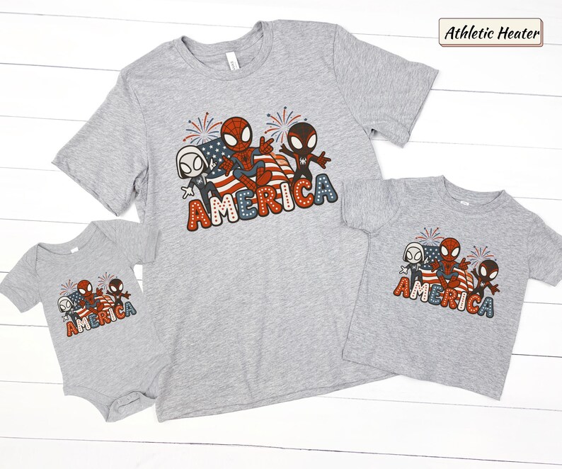 May include: An athletic heather gray t-shirt and matching baby bodysuit featuring a graphic of three cartoon spider characters, a waving American flag, and fireworks. The word AMERICA is printed in large, dotted, red, white, and blue letters.