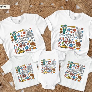 May include: A collection of white t-shirts and a baby bodysuit featuring a colorful graphic print with the text 1776 HAPPY 250 AMERICA 2026. The design includes illustrations of the Statue of Liberty, a bald eagle, a bridge, a taxi, and food items.