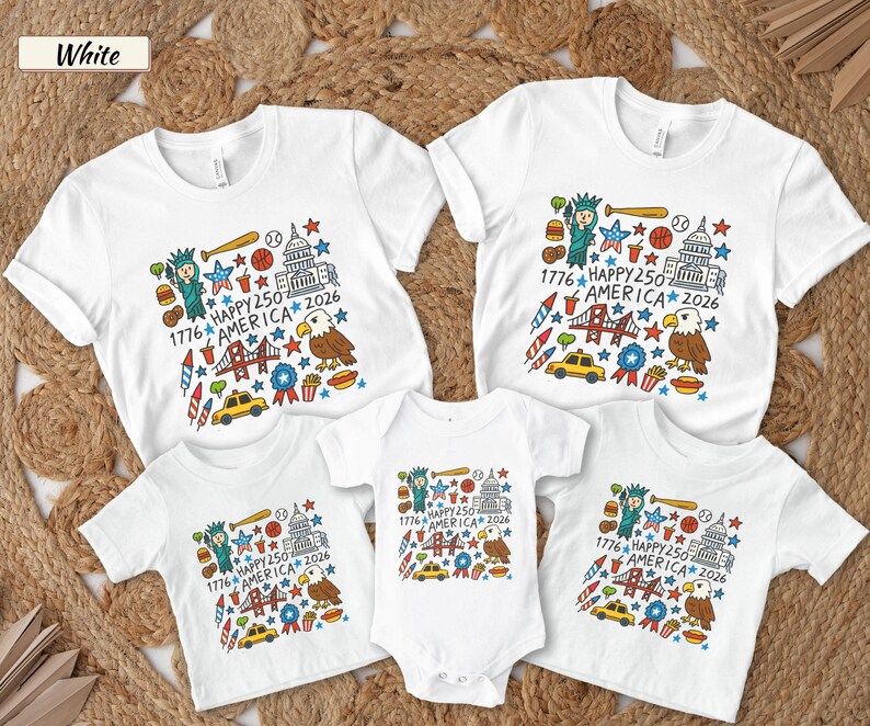 May include: A collection of white t-shirts and a baby bodysuit featuring a colorful graphic print with the text 1776 HAPPY 250 AMERICA 2026. The design includes illustrations of the Statue of Liberty, a bald eagle, a bridge, a taxi, and food items.
