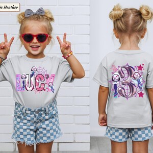 K&ouml;nnte beinhalten: Hellgraues T-Shirt mit dem Namen "LUCY" in rosa und blauen Buchstaben, mit einem Spider-Gwen-Thema. Auf der R&uuml;ckseite des Shirts ist eine gro&szlig;e "3" mit Spider-Gwen-Charakteren und Sternen abgebildet. Getragen von einem jungen M&auml;dchen.