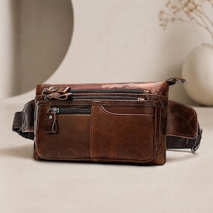 May include: A brown leather fanny pack with multiple zipped compartments and a front pocket. The bag has a wide adjustable strap and a classic, rugged design. The leather has a distressed finish, giving it a vintage look.