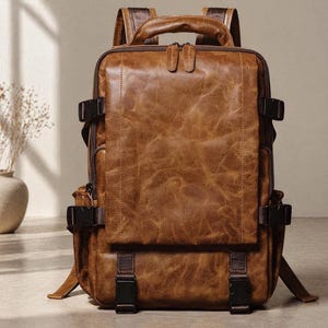 Può includere: Uno zaino in pelle marrone con finitura invecchiata. Lo zaino presenta un manico superiore, spallacci regolabili e scomparti multipli fissati con fibbie e cerniere. La borsa ha una forma rettangolare e un'estetica vintage.