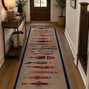 May include: A long rectangular runner rug with a light beige background and a dark blue border. The rug features a repeating pattern of stylized fish in various colors including red, orange, blue, and purple, arranged in rows along the length.