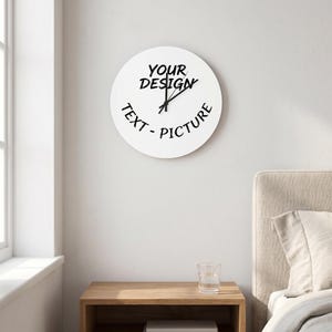 Może przedstawiać: Biały, okrągły zegar ścienny z czarnymi wskazówkami i napisem "YOUR DESIGN" oraz "TEXT - PICTURE". Zegar wisi na białej ścianie, z szafką nocną i oknem w tle.