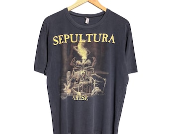 Puede incluir: Una camiseta de manga corta gris carbón con el texto amarillo SEPULTURA en la parte superior y ARISE en la parte inferior. El gráfico central muestra una ilustración detallada, oscura y surrealista de una criatura con un solo ojo.