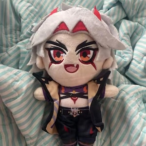 May include: A plush doll featuring a character with white hair, red horns, and detailed facial features. The doll wears a purple and black outfit with gold accents. The doll is approximately 8 inches tall.
