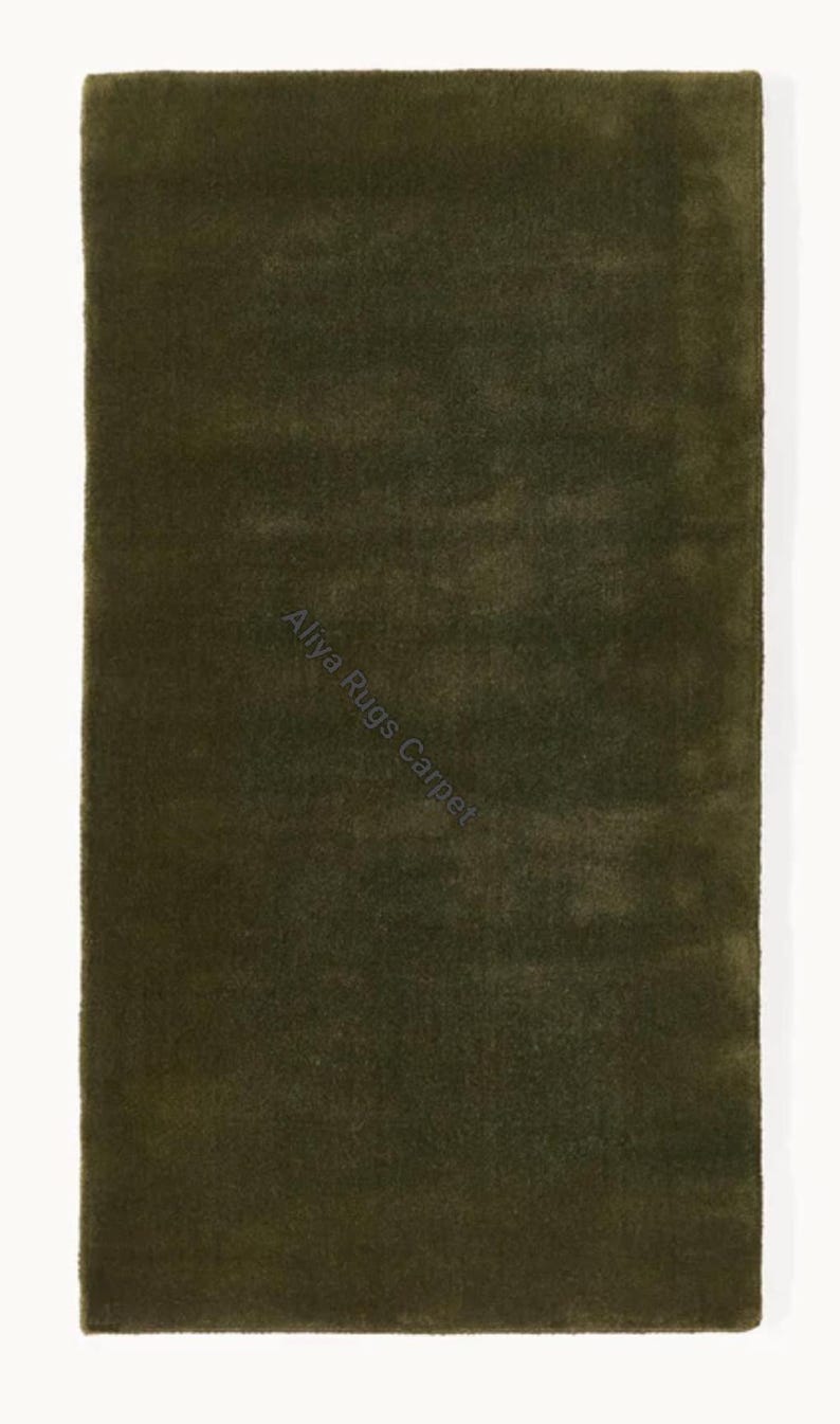 May include: A rectangular, olive green rug with a soft, textured surface. The rug has a solid color and is displayed against a white background. The text "Aliya Rugs Carpet" is visible on the rug.