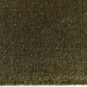 May include: Close-up of a textured, olive green rug. The rug has a dense, plush pile, creating a soft, inviting appearance. The color is a deep, earthy green, suitable for various interior design styles.