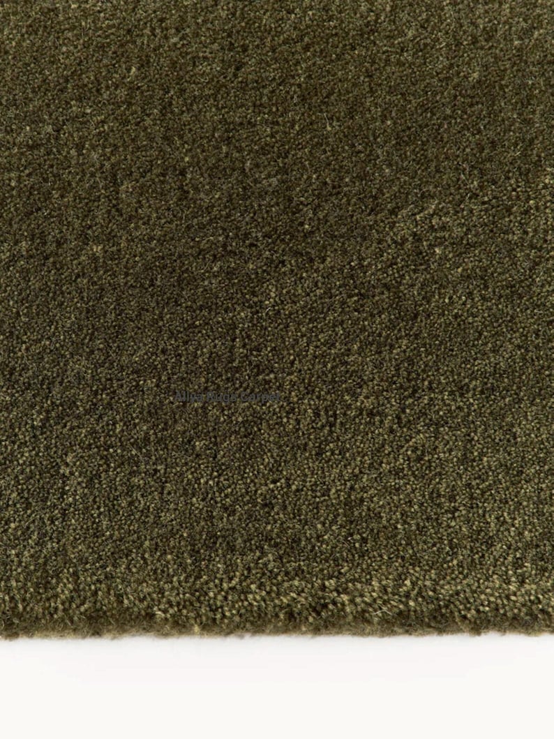 May include: Close-up of a textured, olive green rug. The rug has a dense, plush pile, creating a soft, inviting appearance. The color is a deep, earthy green, suitable for various interior design styles.