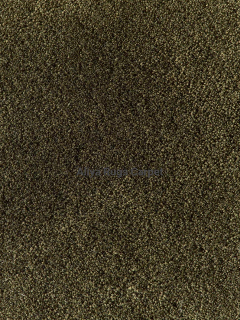 May include: Close-up of a textured, olive-green carpet. The carpet has a dense, short pile, creating a soft, uniform appearance. The color is a muted, earthy tone, suitable for various interior design styles.
