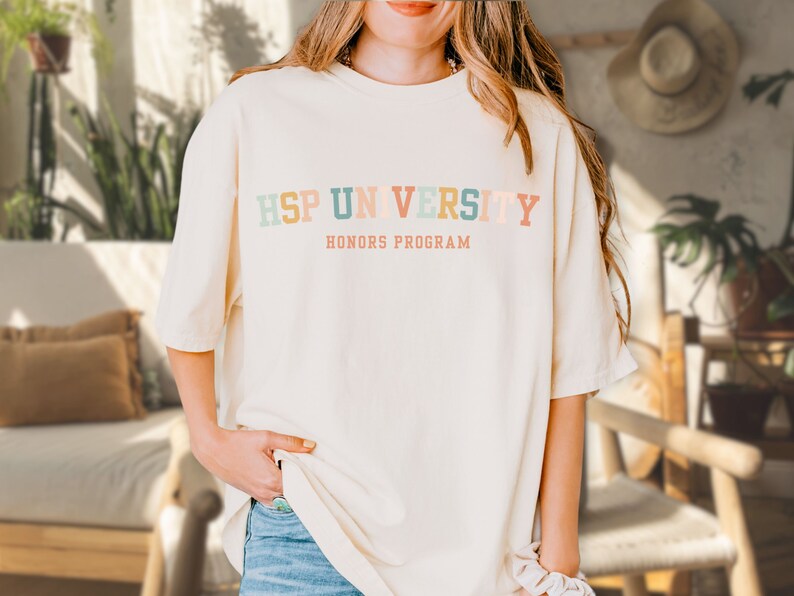 K&ouml;nnte beinhalten: Ein wei&szlig;es T-Shirt mit dem Text "HSP UNIVERSITY HONORS PROGRAM" in bunten Buchstaben.
