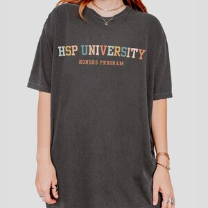 K&ouml;nnte beinhalten: Ein schwarzes T-Shirt mit dem Text "HSP UNIVERSITY HONORS PROGRAM" in bunten Buchstaben.