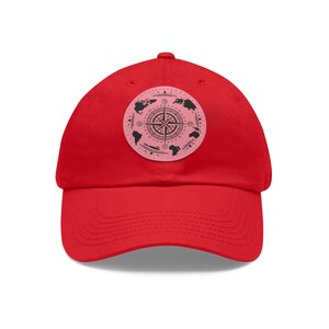 May include: A vibrant red baseball cap with a circular patch displaying a compass rose design. The patch features black world map outlines on a pink backdrop. The cap is made of a soft material, suitable for various head sizes.