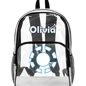Może przedstawiać: Biało-czarny plecak z przezroczystym panelem przednim. Imię "Olivia" jest wydrukowane na górze na jasnoniebiesko. Niebiesko-biała grafika jest wyśrodkowana na przednim panelu. Plecak ma czarne wykończenia i czarny uchwyt.