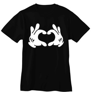 May include: A black short-sleeved t-shirt featuring a large white graphic print on the chest. The graphic depicts two cartoon-style gloved hands positioned together to form a heart shape, with three distinct lines on each glove wrist.