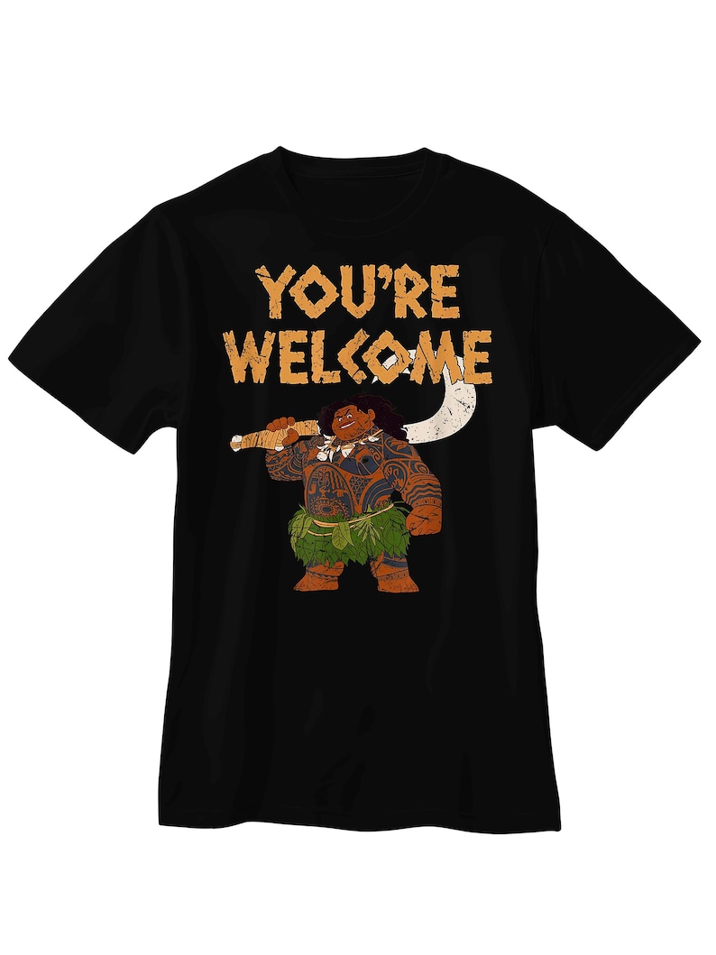 Puede incluir: Una camiseta negra de manga corta con un gr&aacute;fico de un personaje grande y musculoso con tatuajes tribales marrones, que lleva una falda de hojas verdes y sostiene un gran gancho blanco. El texto YOU'RE WELCOME est&aacute; impreso en naranja arriba.