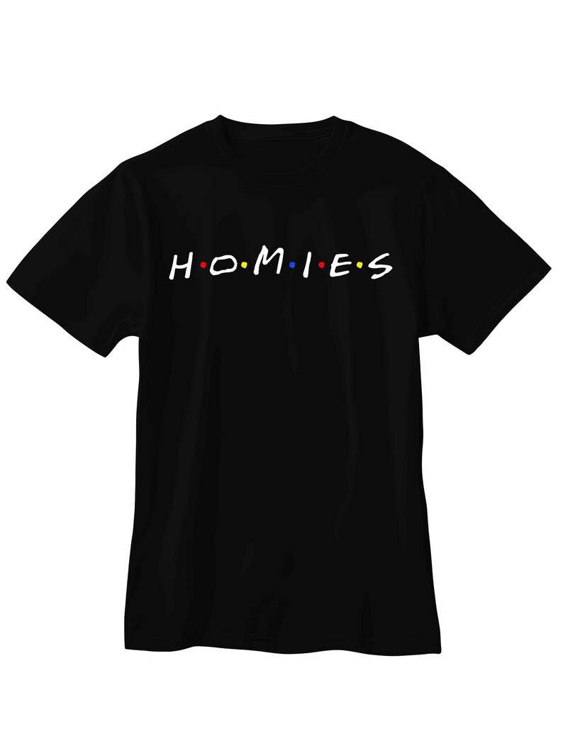 May include: A black short-sleeved t-shirt featuring the white text "H.O.M.I.E.S" printed across the chest. The letters are separated by small colored dots in red, blue, and yellow, mimicking a classic television show logo style.