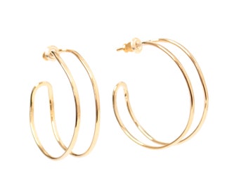 May include: A pair of gold-toned hoop earrings, each featuring a double-layered design with two thin, concentric circular wires. The earrings are finished with a small post and backing mechanism for secure attachment to the earlobe.